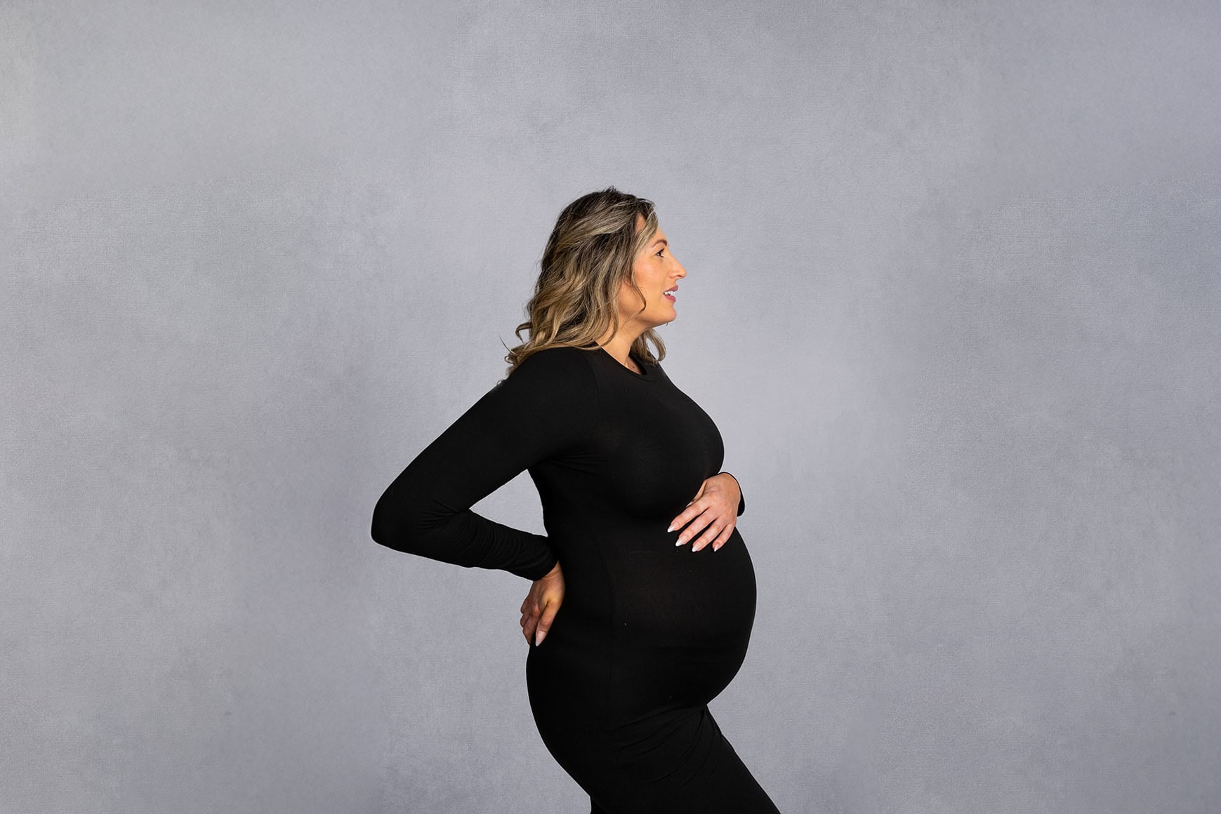 Studio portrait side profile of an expectant mum, with one hand rested on her bump and the other on her lower back