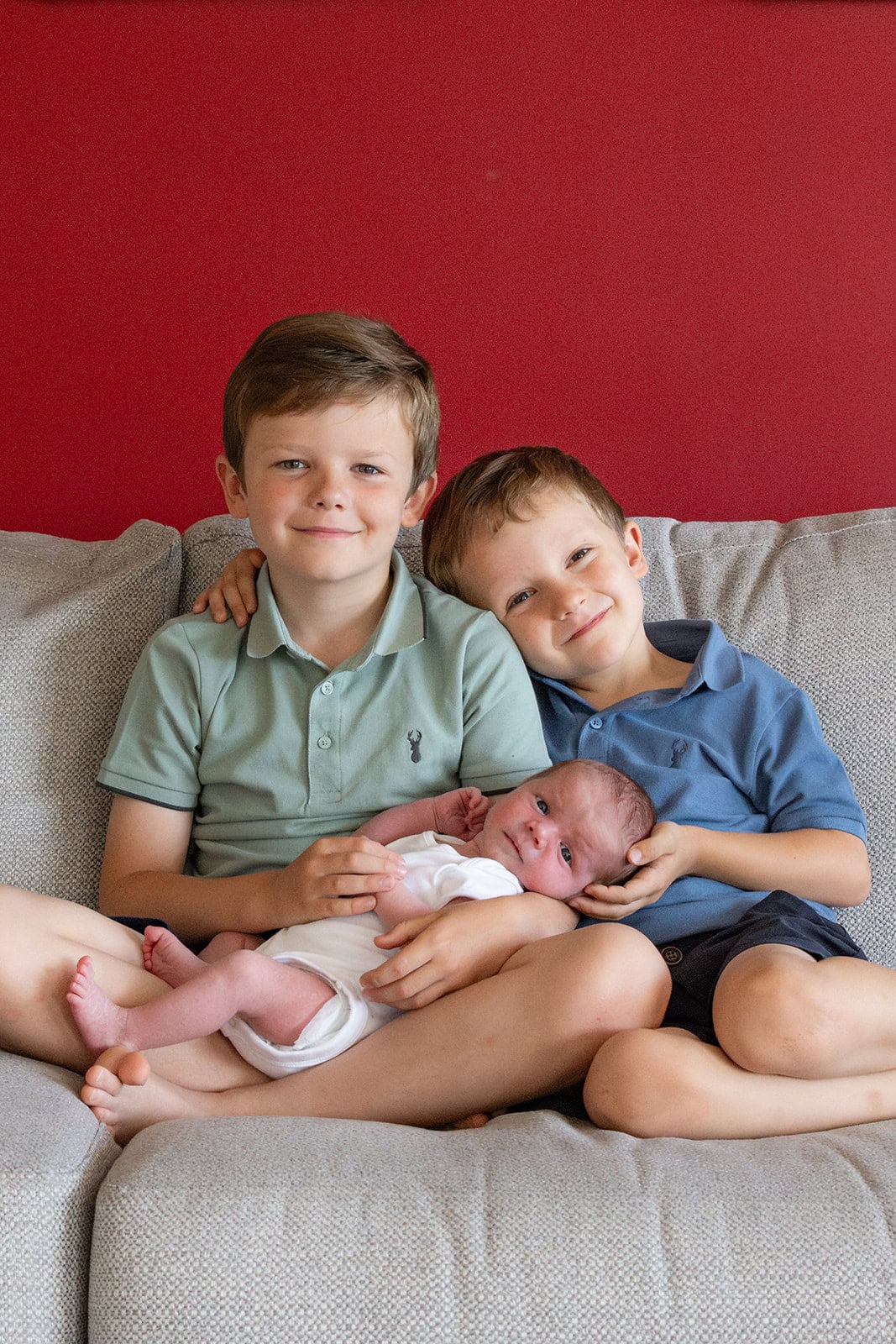 Two brothers hold their new sibling during a newborn photoshoot in Berkhamsted